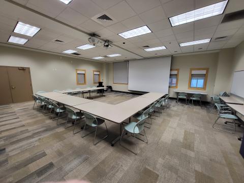 Community Room with tables and chairs arranged in u-shape around the projector